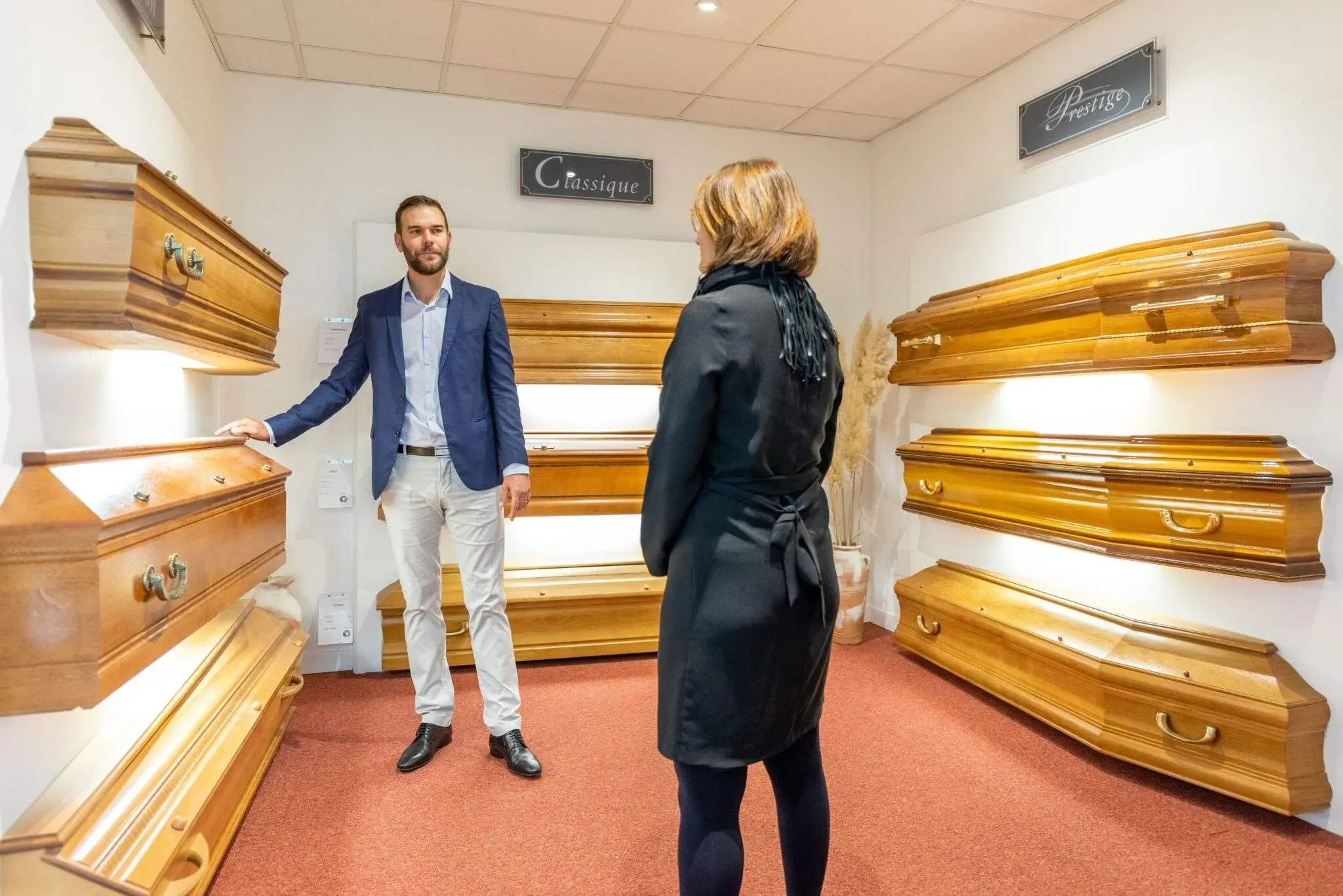 Conseiller présentant des modèles de cercueils en bois à une cliente.